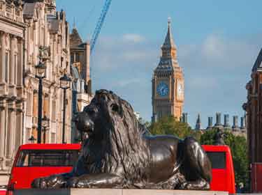 Lion Statue and iconic red bus in Trafalgar Square, London, with Big Ben on the background